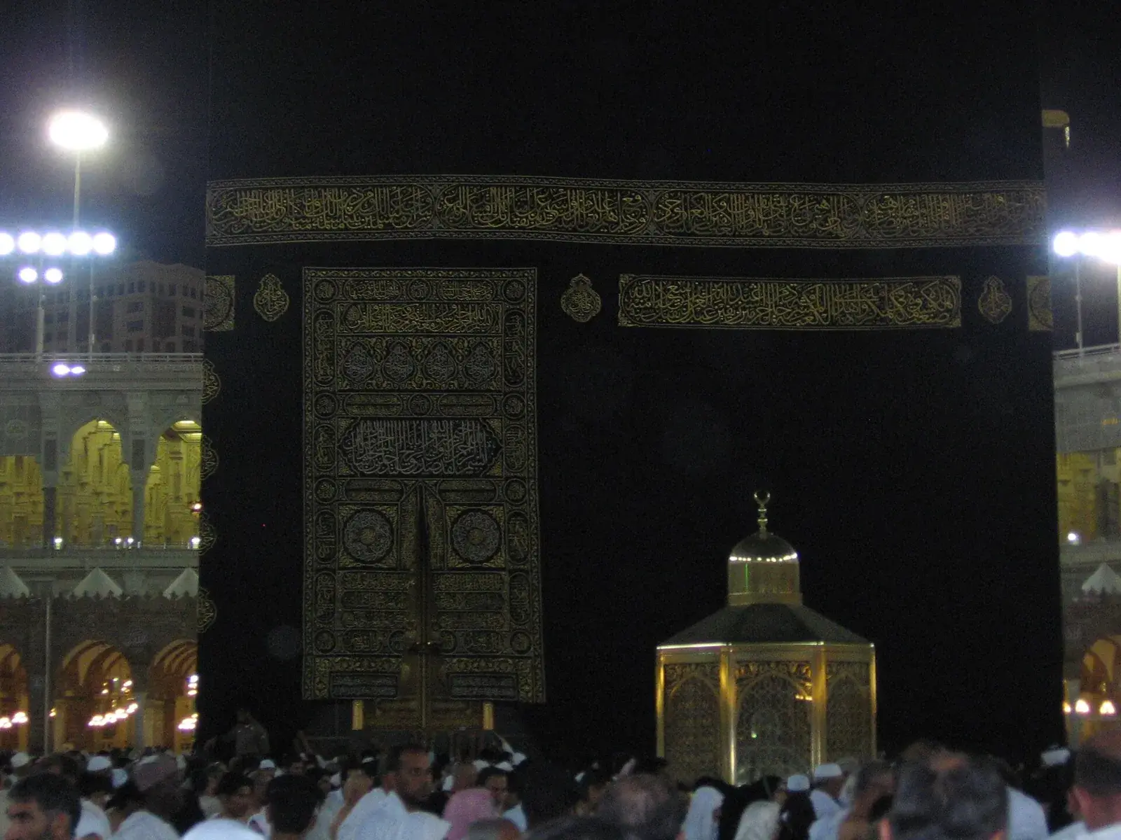 The gold-toned glass enclosure of Maqam Ibrahim standing on the marble floor near the Kaaba