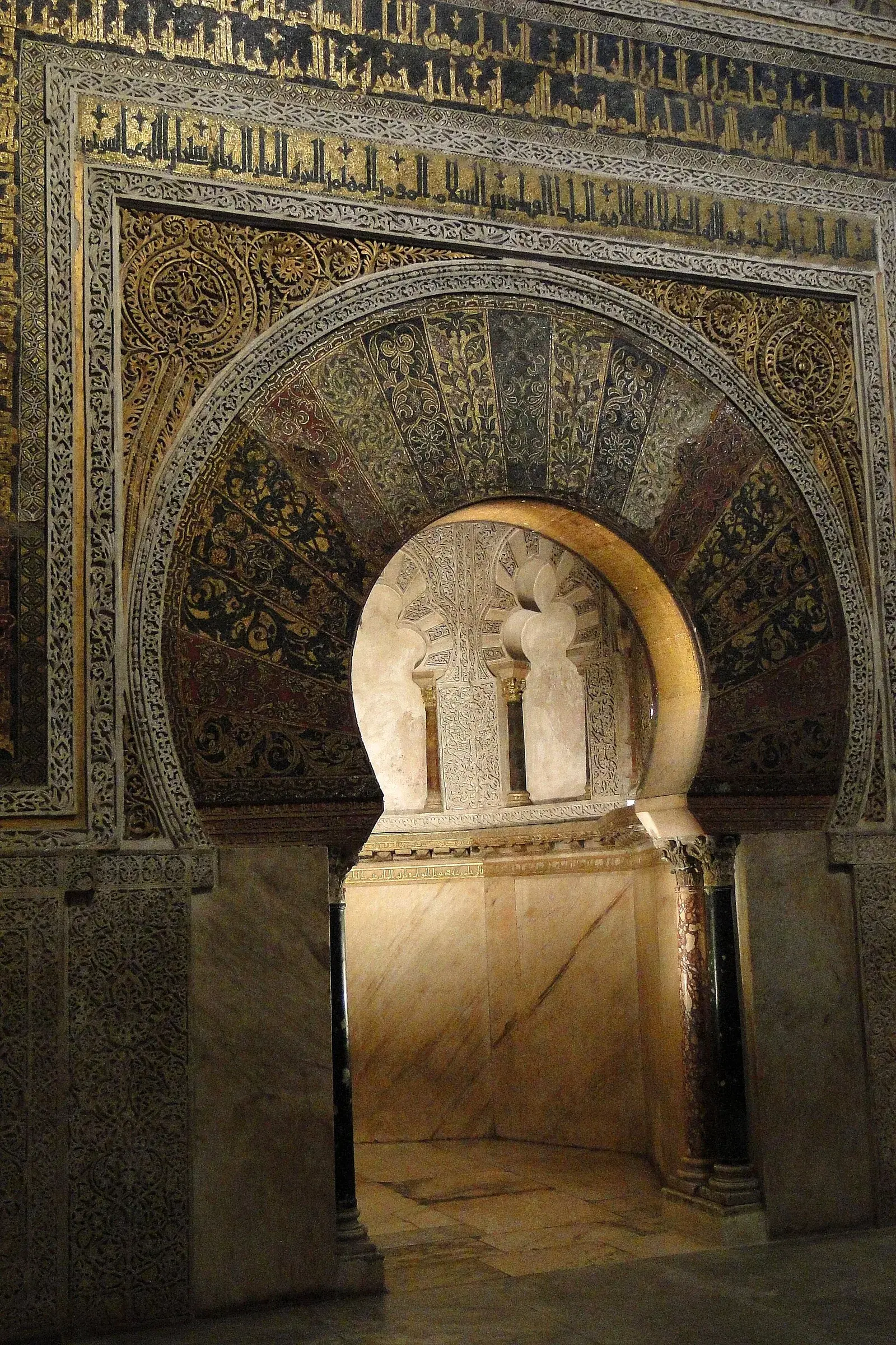 An ornately decorated mihrab niche set into the wall of a mosque prayer hall