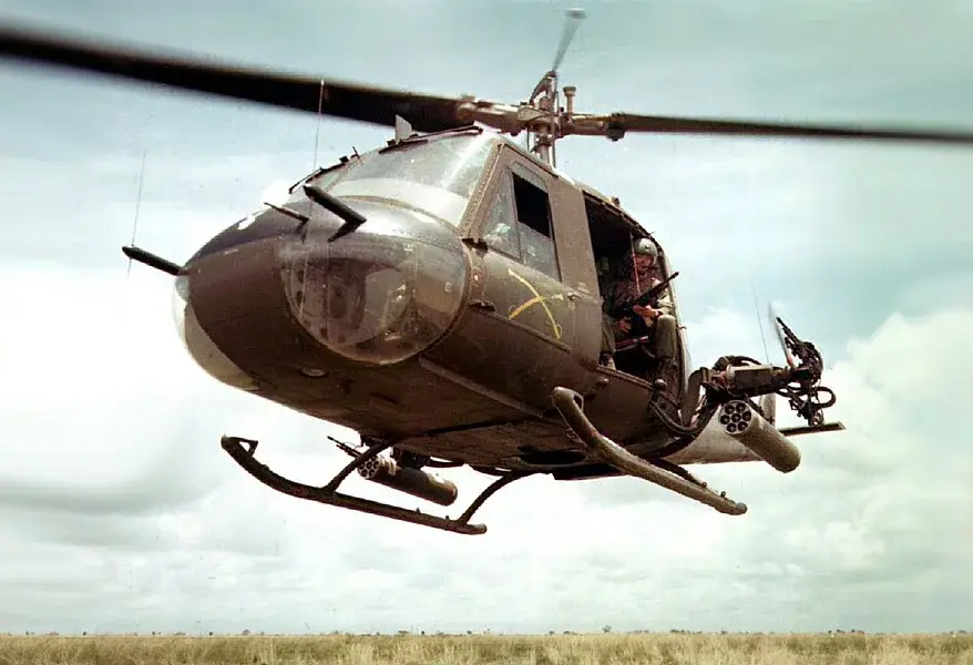 A military helicopter flying low over green rice paddies and a winding river