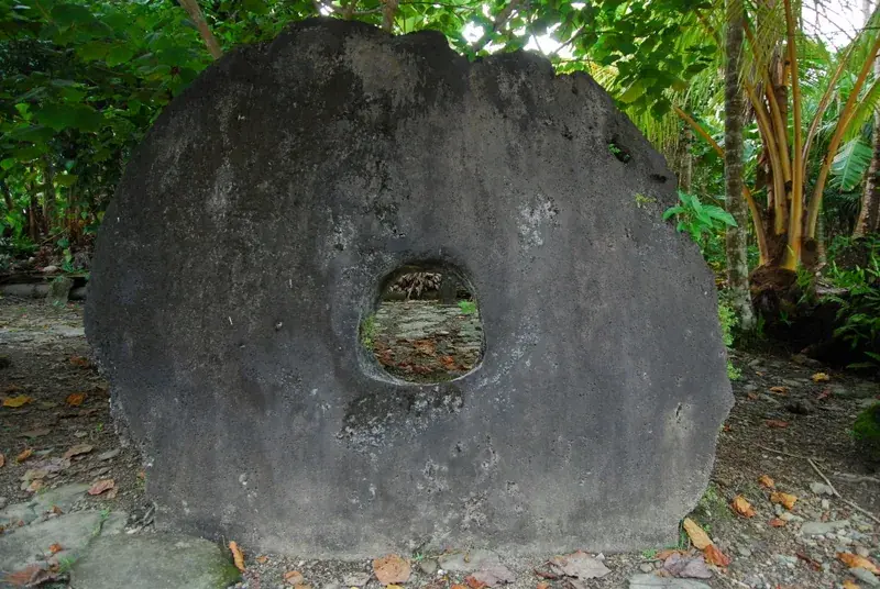 Large carved limestone discs of Yapese rai stone money leaning in a row beneath palm trees