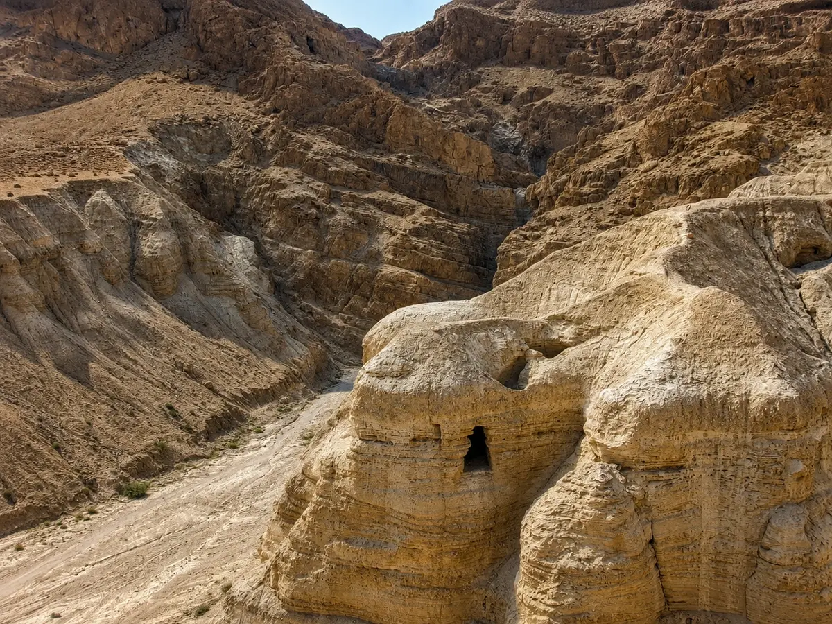 Two dark openings cut into a pale marl cliff face above the Qumran ravine